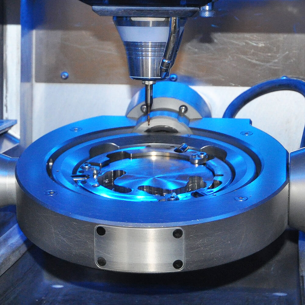 Nahaufnahme einer CAD-CAM-Fräseinheit mit Frässpindel und Metallaufnahme im blau beleuchteten Maschinenraum.
