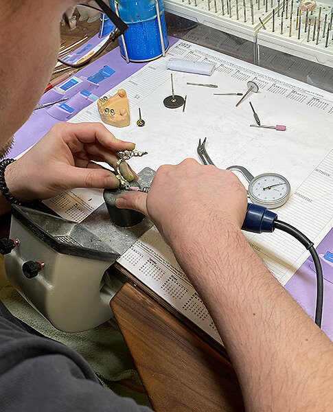 Zahntechniker arbeitet mit Präzisionswerkzeug an einem kleinen zahntechnischen Werkstück auf dem Labortisch.