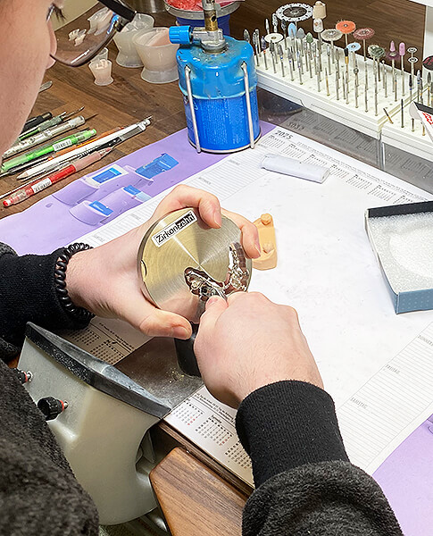 Zahntechniker bearbeitet eine Metallprothese mit Werkzeug an einem Laborarbeitsplatz.