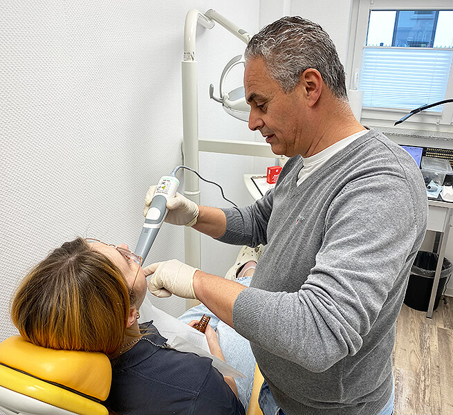 Zahntechniker führt einen digitalen Intraoralscan bei einer Patientin im Behandlungsstuhl durch.