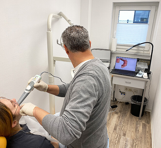 Digitaler Intraoralscan bei einer Patientin mit Monitoransicht des gescannten Zahnmodells im Behandlungsraum.