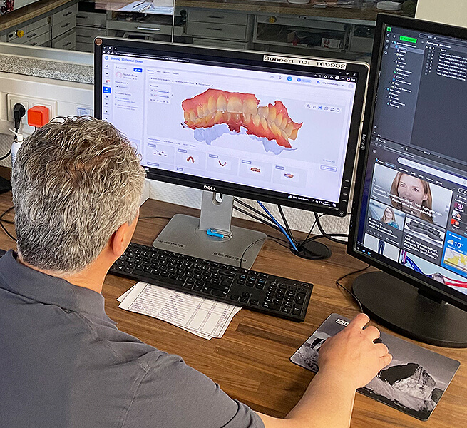 Zahntechniker bearbeitet einen digitalen Zahnscan am Computerarbeitsplatz im Dentallabor.
