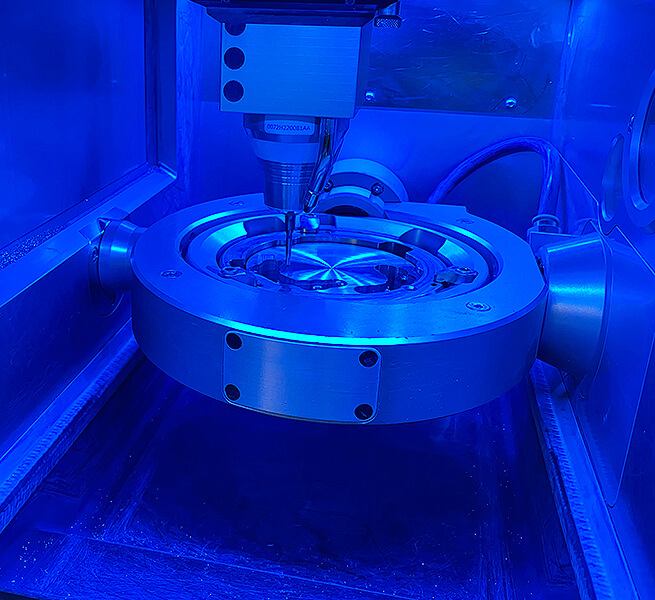 Blau beleuchtete CAD-CAM-Fräsmaschine während der präzisen Bearbeitung eines zahntechnischen Werkstücks.