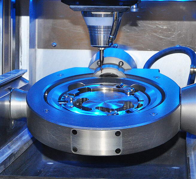 CAD-CAM-Fräsmaschine mit eingespanntem Fräsrohling und Fräswerkzeug im blau beleuchteten Innenraum.