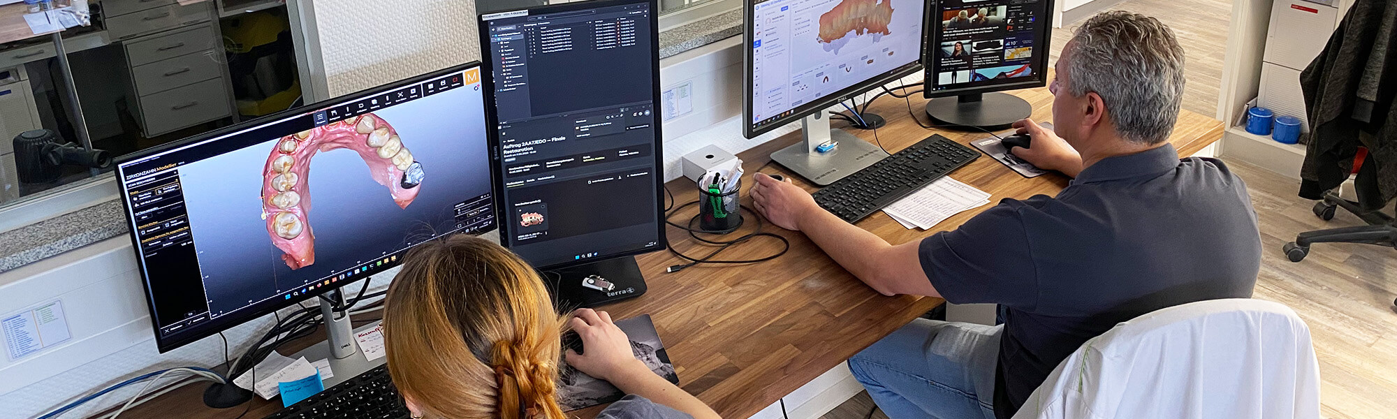 Zahntechniker bei der digitalen CAD-Konstruktion von Zahnersatz an mehreren Computerarbeitsplätzen im Dentallabor.