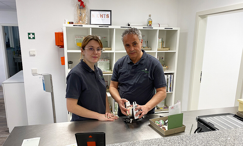 Zwei Zahntechniker im Dentallabor mit Zahnmodell und zahntechnischen Arbeiten auf dem Labortisch.