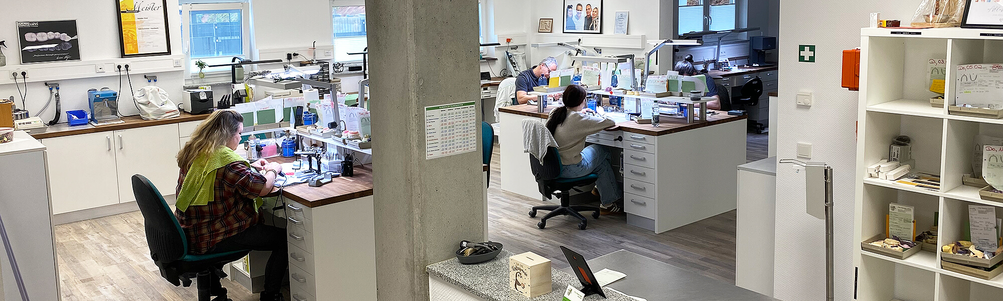 Innenansicht eines modernen Dentallabors mit mehreren Arbeitsplätzen und Zahntechnikern bei der Arbeit.